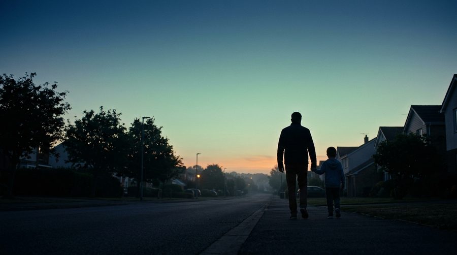 Siluet ayah dan anak laki-laki berjalan bersama di jalan tenang saat fajar dengan langit gradasi lembut